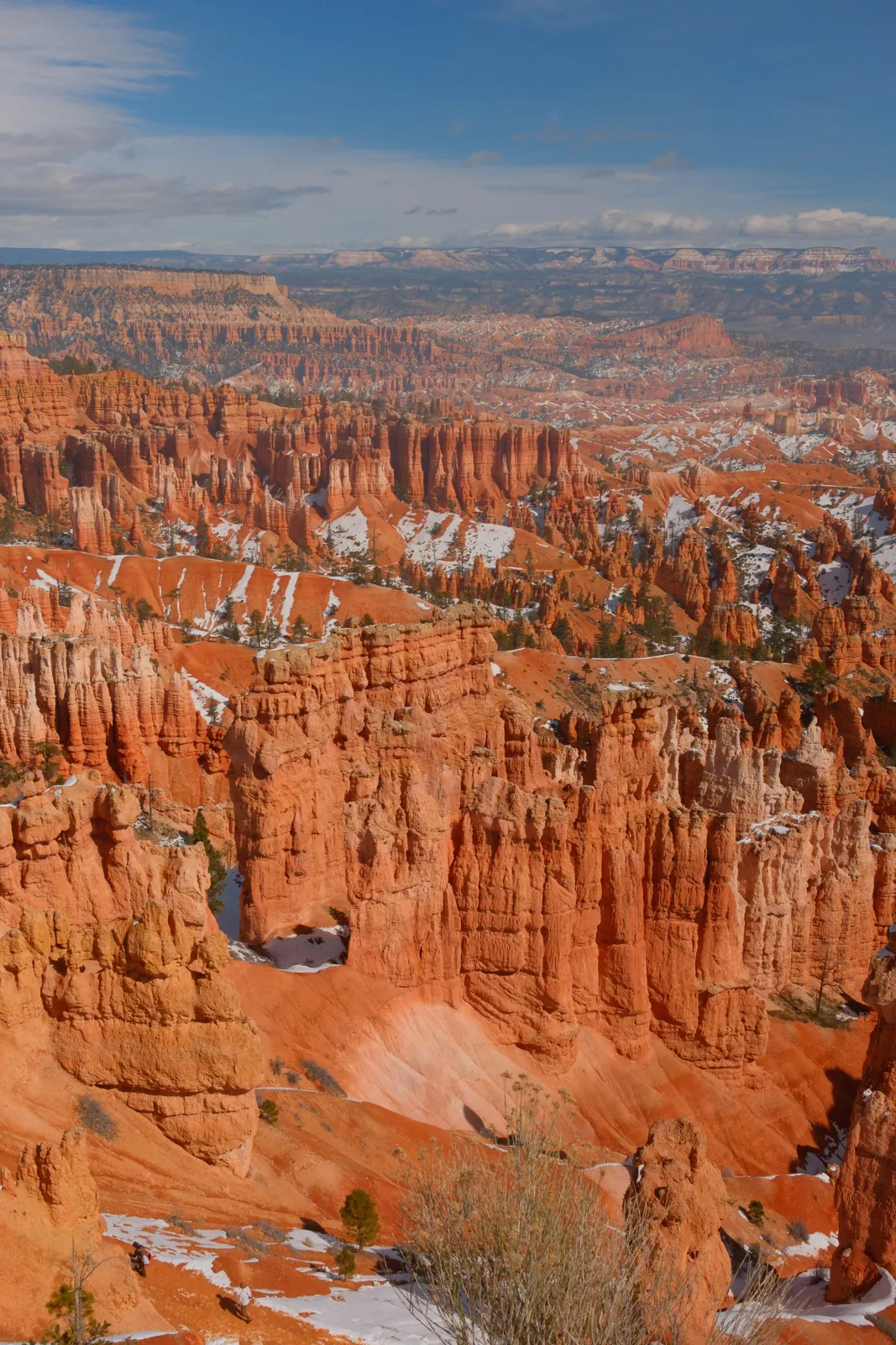 A vast landscape of orange hoodoos with patches of snow under a bright blue sky.
