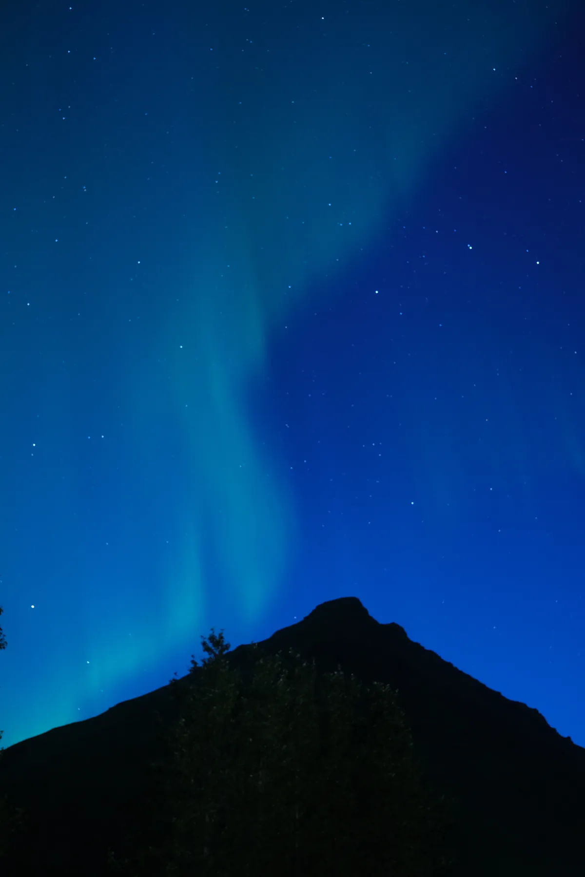 The aurora borealis illuminates the night sky above a dark mountain.