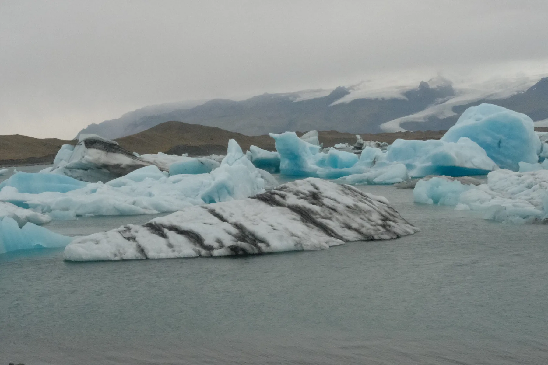 Large icebergs float in a glacial lagoon under a cloudy sky.